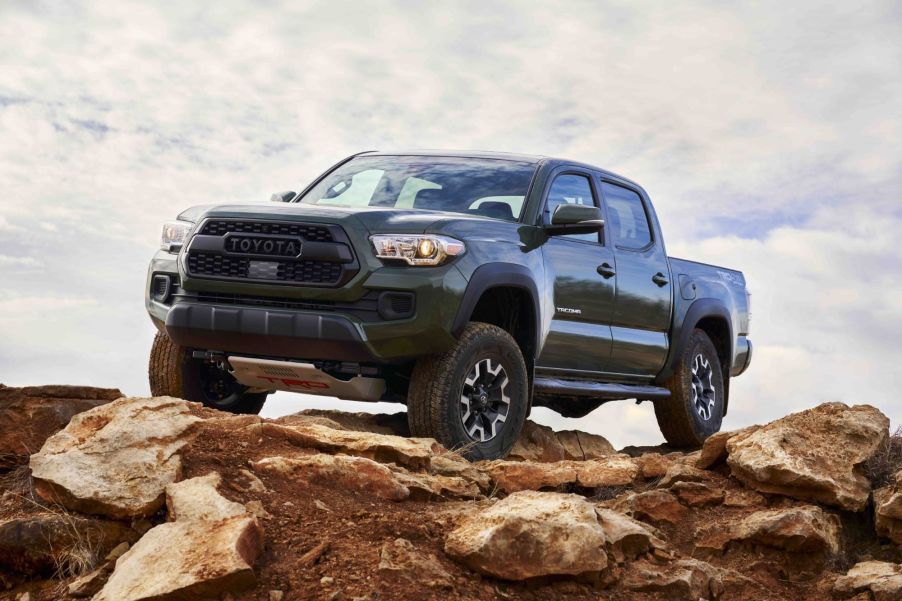 A dark green 2021 Toyota Tacoma sitting on top of a brown rocky terrain with a cloud covered background.