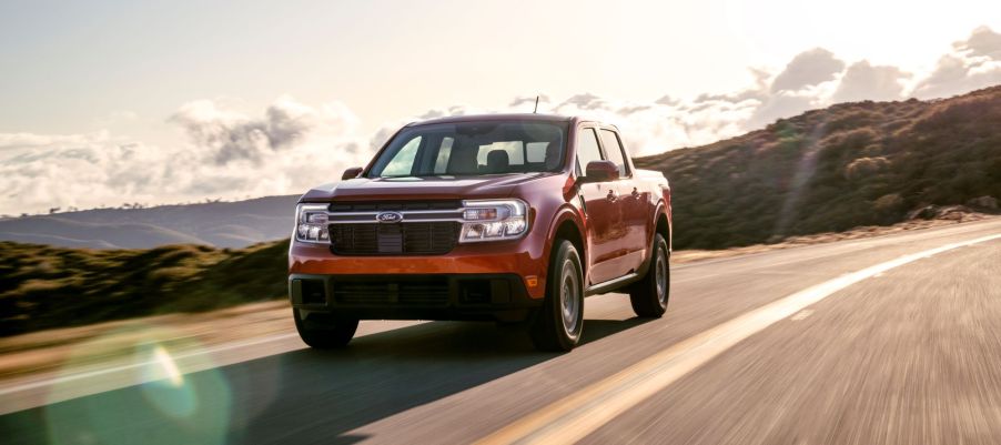 The 2022 Ford Maverick Lariat truck model with an orange paint color driving on a country highway