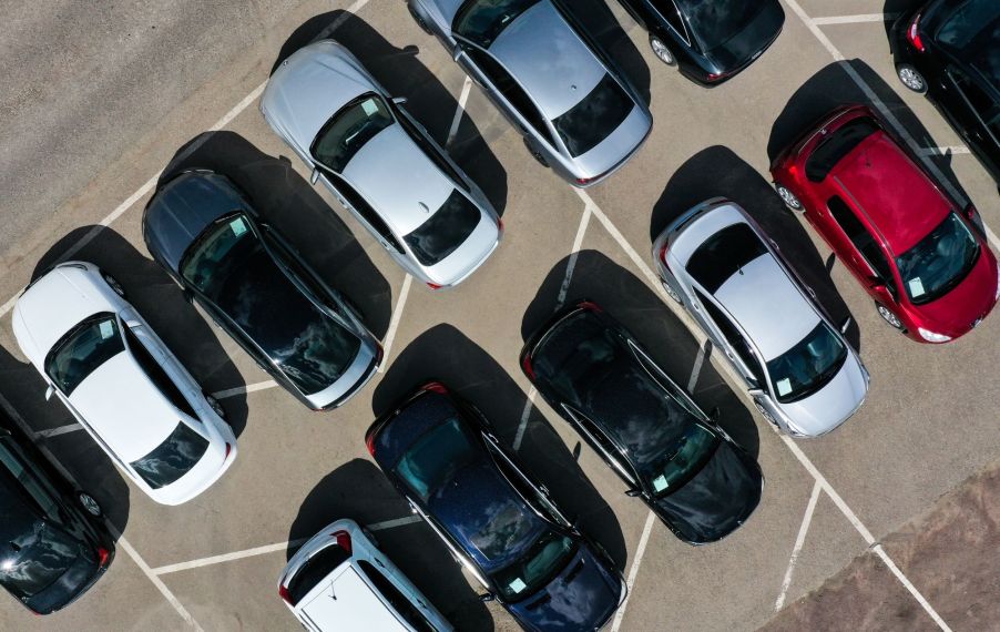 A group of cars in a dealership parking lot ranging in colors from black, red, and silver.