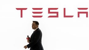 Tesla CEO Elon Musk presents at a conference with the brand's logo seen in red on a white background behind him