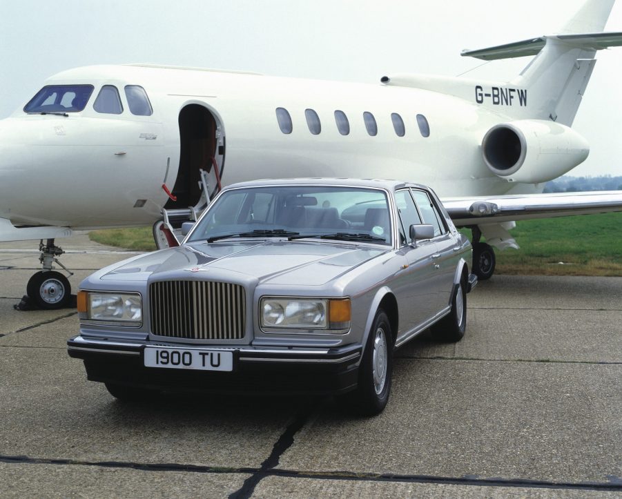 A Bentley Turbo R sits beside a private jet on a runway