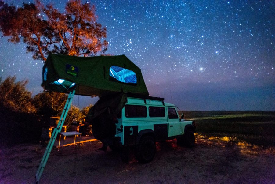 A Land Rover with a roof tent parked under the stars