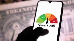 A photo illustration of a hand holding a smartphone showing a graph with the credit score