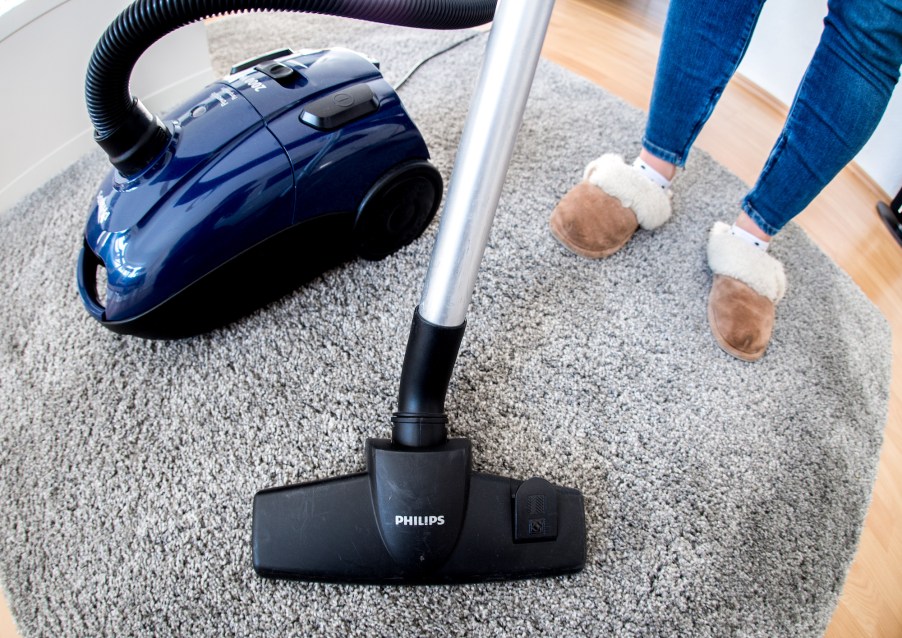 A woman in an apartment uses a vacuum cleaner on carpeting