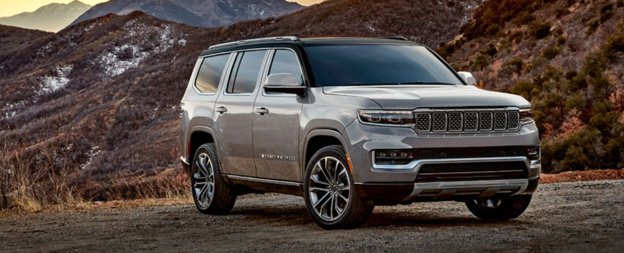 The Jeep Grand Wagoneer luxury SUV parked on a dirt trails near grassy hills and mountains