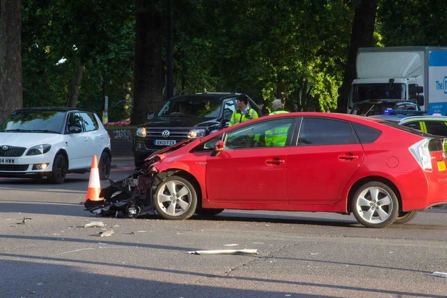 A badly damaged red Toyota Prius in the middle of the road after an accident.