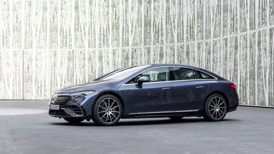 A blue 2022 Mercedes-Benz EQS on a concrete surface in front of a white and grey background.