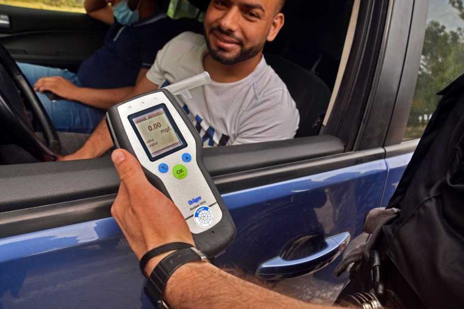 A police officer performs an alcohol breath test of a driver of a blue car