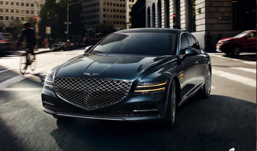 A dark colored 2021 Genesis G80 driving through a city.