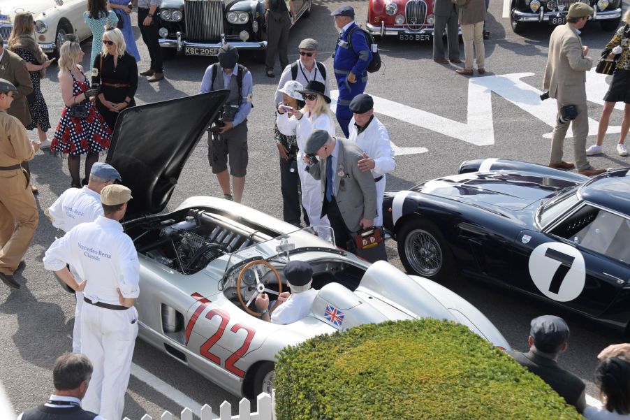 Onlookers in vintage clothing look at classic cars at the 2021 Goodwood Revival, including Sir Stirling Moss's silver No. 722 1955 Mercedes-Benz 300 SLR