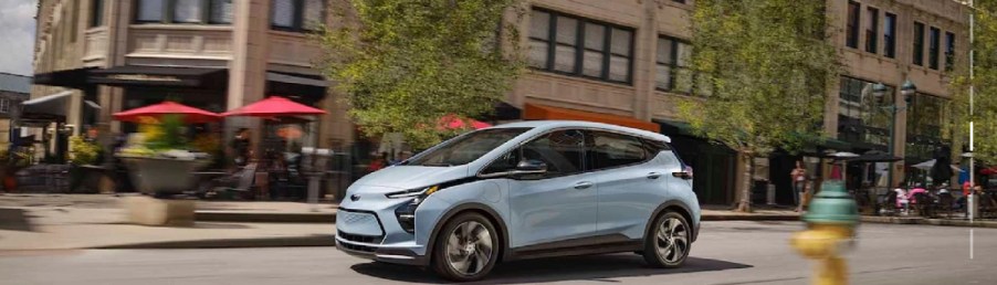 An ice blue 2022 Chevy Bolt driving through a city.