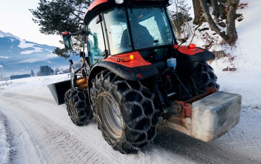 A tractor driving on a snowy road with with snow chains on its tires