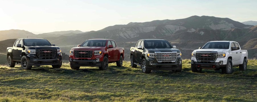 Four GMC pickup trucks parked in front of mountains.