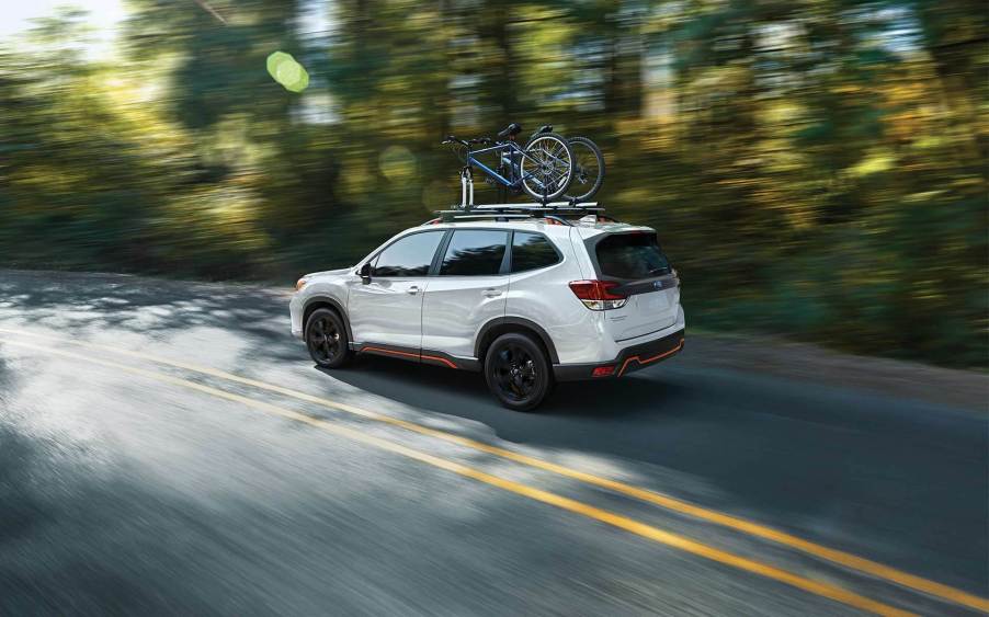 A white 2021 Subaru Forester speeding down a tree-lined road.