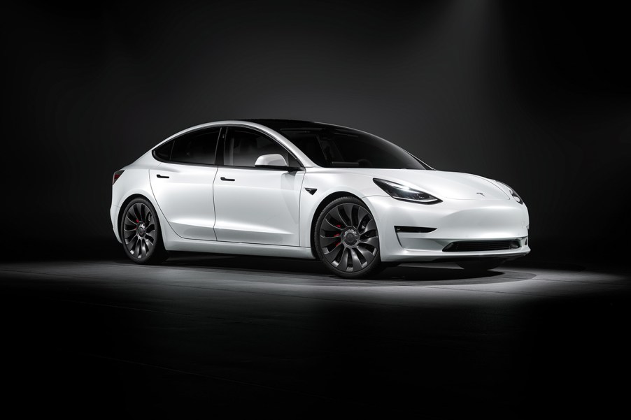 A white Tesla Model 3 facing toward the right in a black photo studio