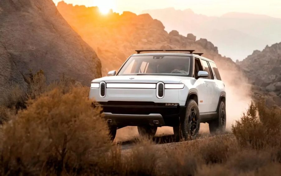 White Rivian R1S electric SUV driving by a large rock