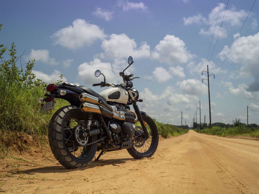 A low-angle rear 3/4 view of a white 2022 Triumph Street Scrambler on a dirt road