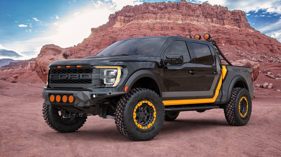 A 2022 Ford F-150 Raptor in a dark grey color with a light grey and yellow racing stripe graphics. The truck is lifted with off road wheels and tires. The wheels have bead locks that are yellow and color matched to the graphics. This truck will be on display at SEMA 2021