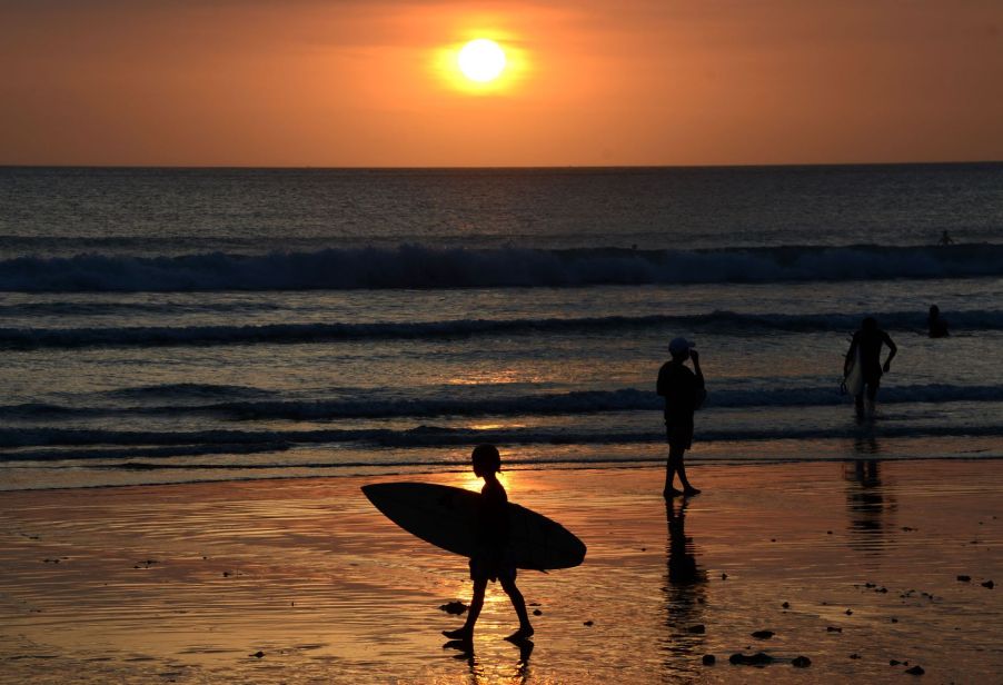 People on Kuta Beach in Bali, Indonesia as the sun sets over the ocean