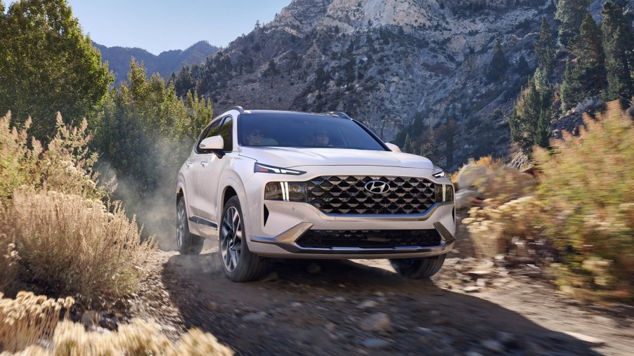 A white 2022 Hyundai Santa Fe driving down a wooded road.