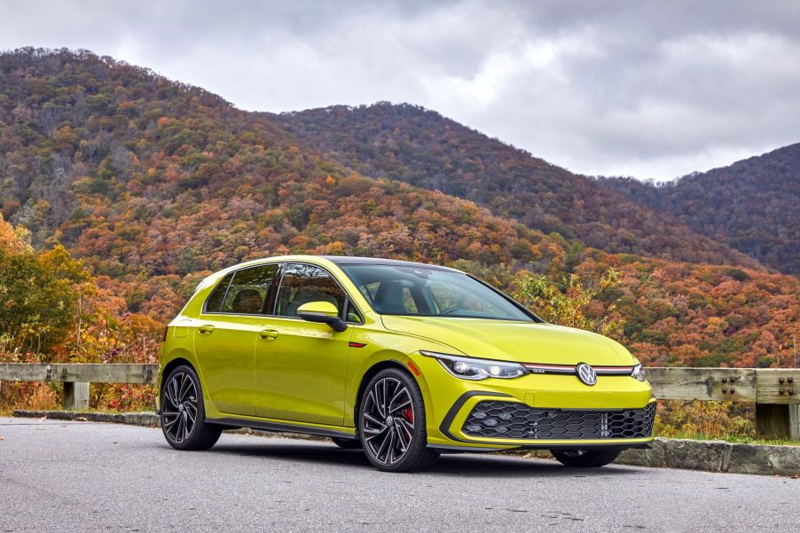 A 2022 Volkswagen Golf GTI hot hatch with a bright yellow paint color option parked near a forest of autumn trees