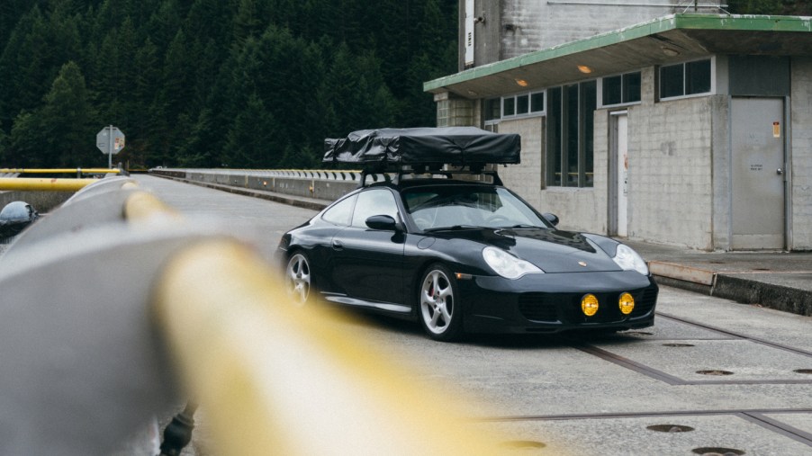 A dark green 996 Porsche 911 sports car sporting a roof tent and rally lights