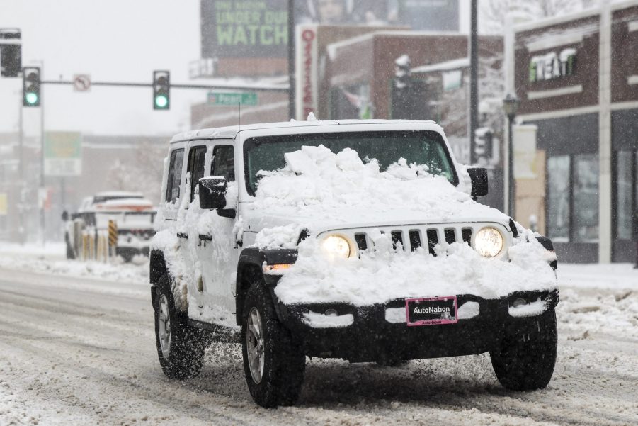 A white Jeep Wrangler driving through the snow in Denver, Colorado