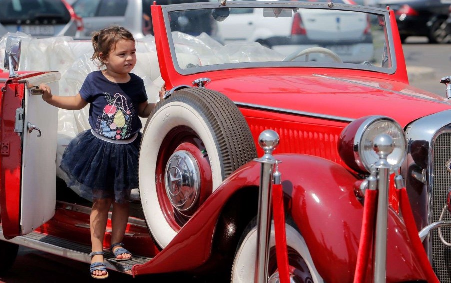 A child standing by the door of an antique, car, thinking about a car book for kids Christmas gift