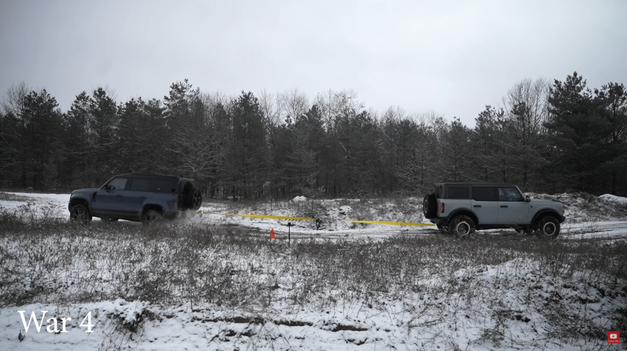 A 2022 Ford Bronco and Land Rover Defender playing tug of war in the snow, off-road SUV battle.