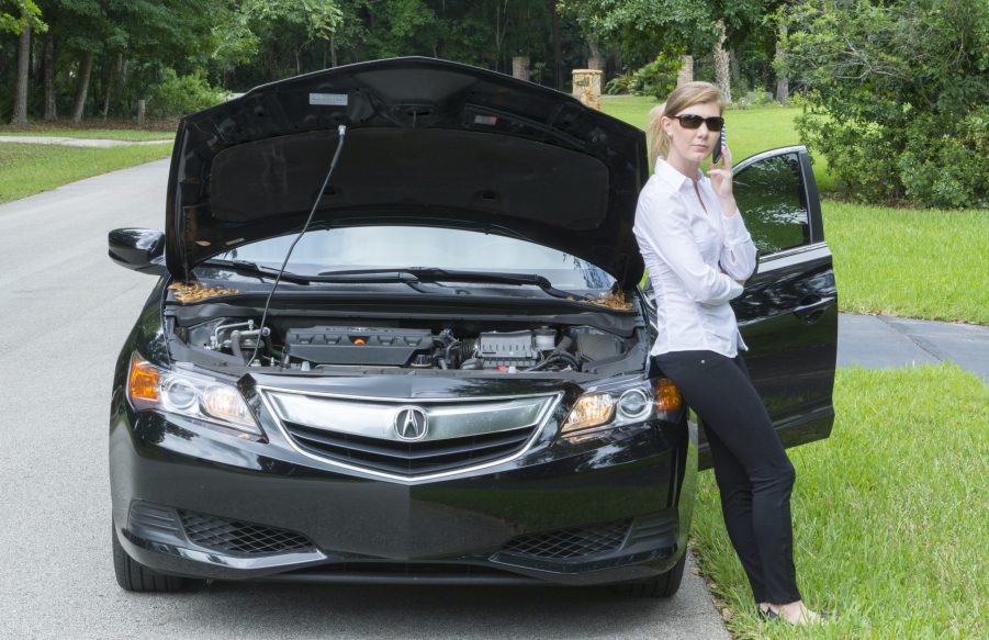 Young woman with car broken down on side of road using cell phone