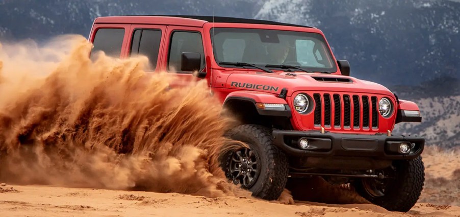 A red 2022 Jeep Wrangler spraying sand.