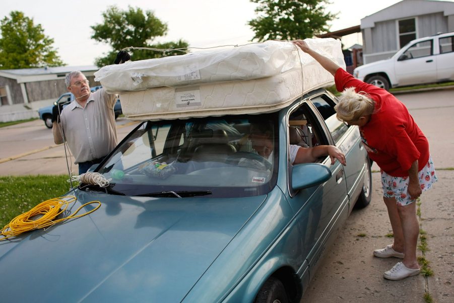 an older couple straps a mattress to a car roof