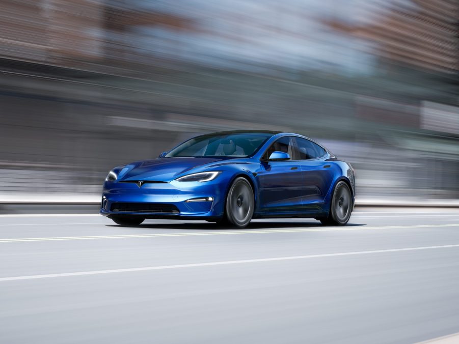 A 3/4 front view of a blue 2022 Tesla Model S driving on a street with a blurred background.