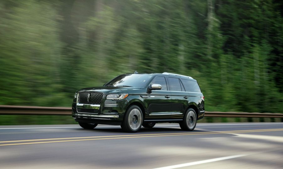 2022 Lincoln Navigator Black Label full-size luxury SUV in Manhattan Green driving on a highway past of a forest of evergreen trees