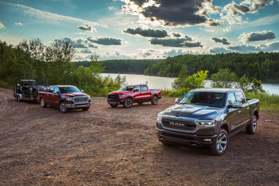 Three 2022 Ram 1500 pickup trucks parked on a dirt road in front of a farm.