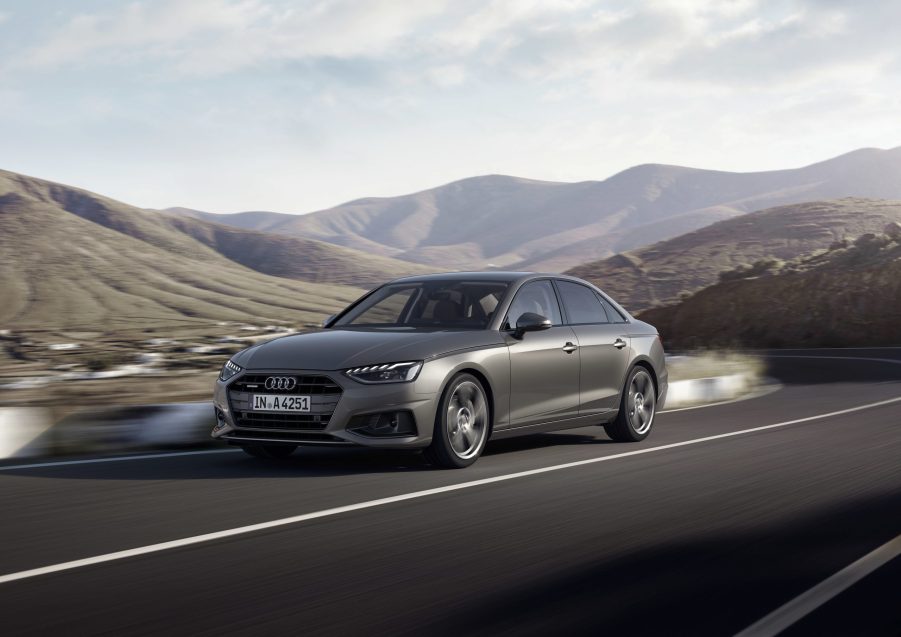 A 3/4 front view of a gray Audi A4 sedan driving on a road with hills in the background.