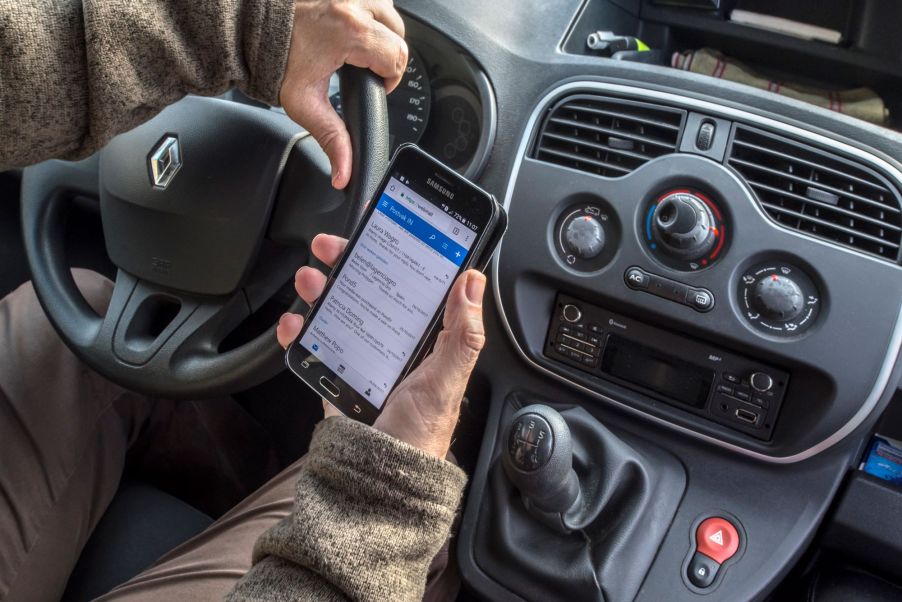 A man being a distracted driver by watching his phone rather than the road, which is a bad driving habit.