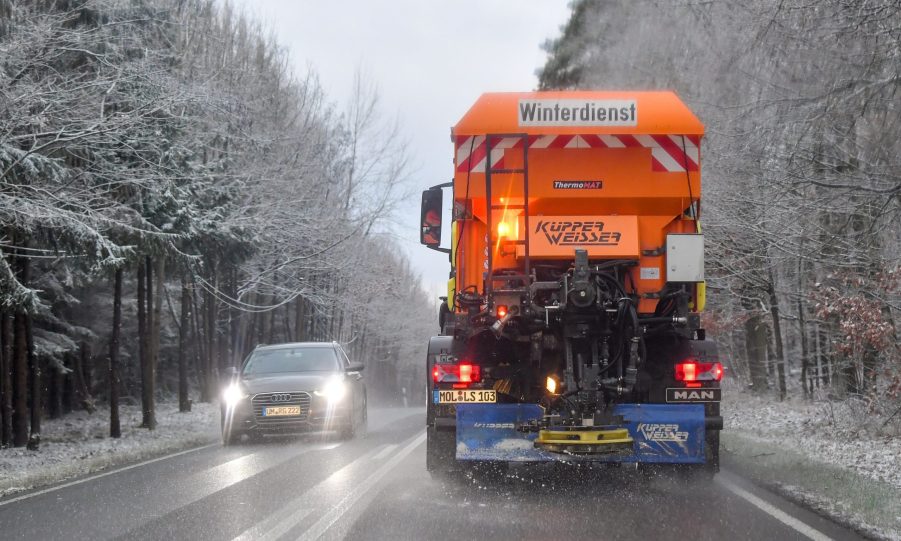 A snow plow spreads road salt over a snowy road