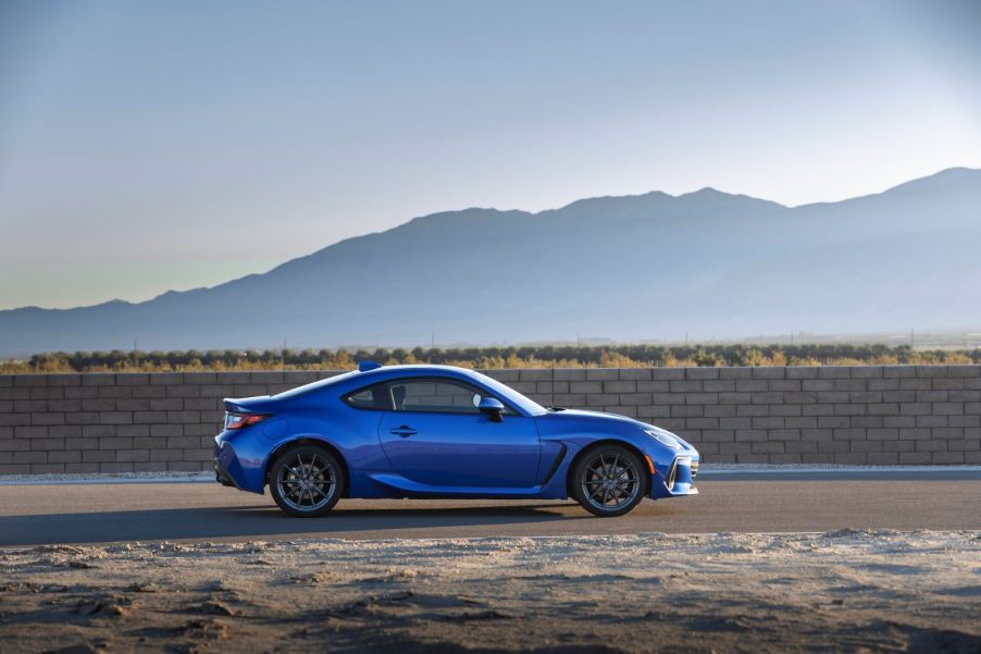 Side profile of a blue 2022 Subaru BRZ coupe, trim level uncertain, parked on a dirt road against the backdrop of sprawling mountains