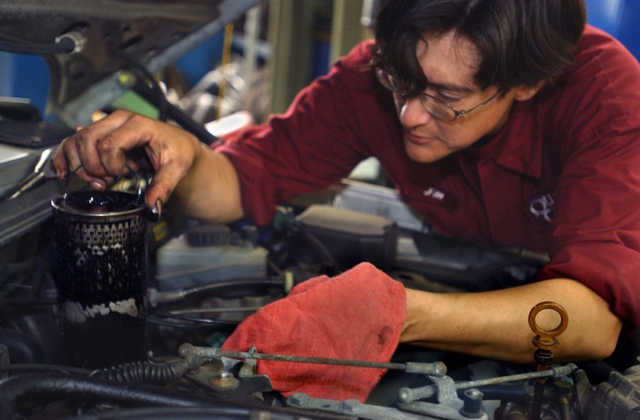 A red-clothed mechanic replaces the oil filter on a 1985 Mercedes-Benz