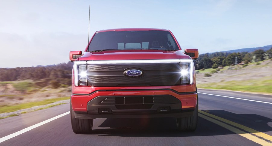 A red 2022 Ford F-150 Lightning is driving down the road.