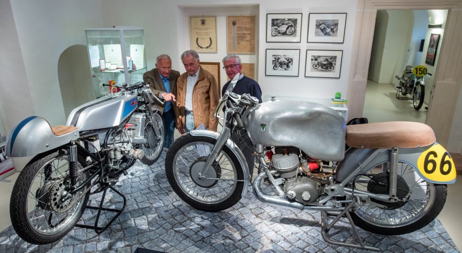 Norbert Kaaden, Christian Steiner, and Lutz Langer next to a MZ RD 125 (left) and a a DKW 350 RM at a two-stroke motorcycle show honoring Walter Kaaden