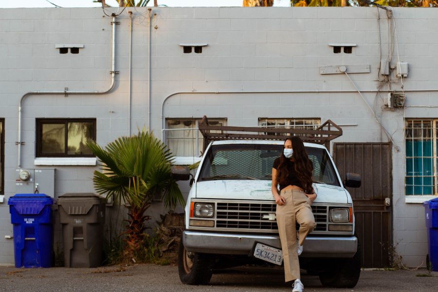 Young diesel enthusiast and her white Chevy truck parked by a building.