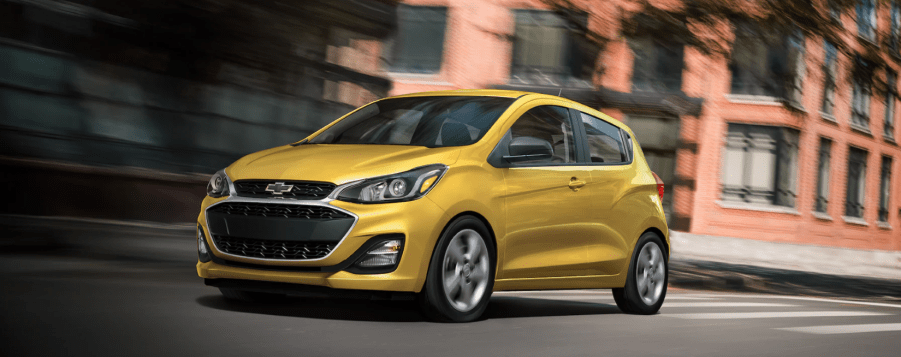 The 2022 Chevy Spark subcompact hatchback in yellow driving through an urban cityscape