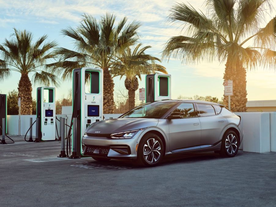 A silver 2022 Kia EV6 parked at charging stations surrounded by palm trees.