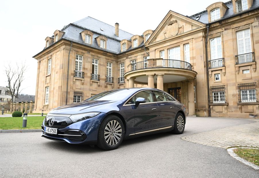 A blue 2022 Mercedes-Benz EQS in front of a large brown brick house.