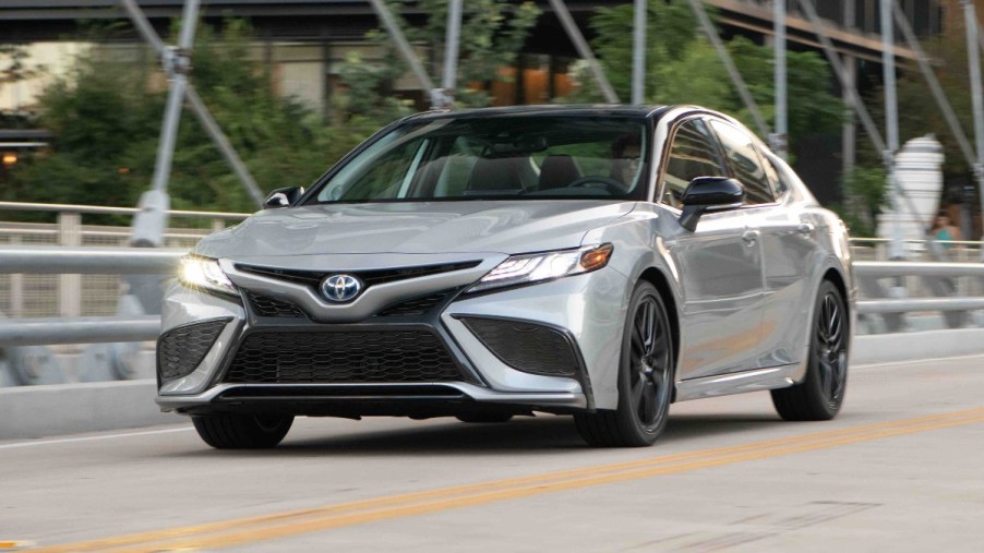 A silver 2022 Toyota Camry Hybrid drivers over a bridge with its LED lights on