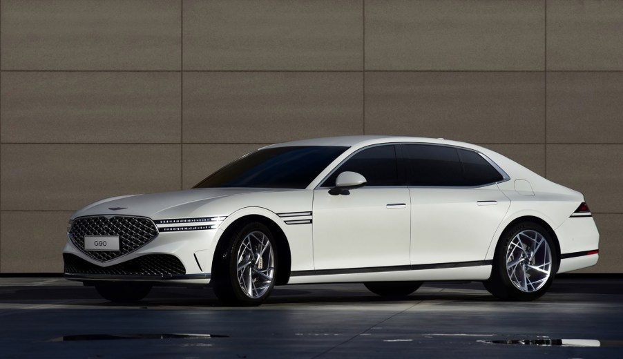 A white 2023 Genesis G90 next to a brown stone wall