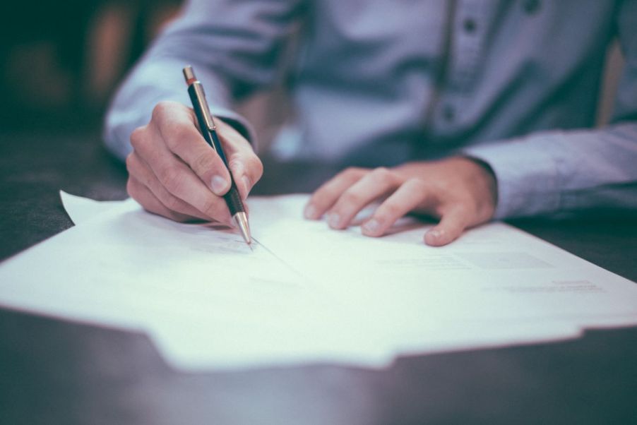 A white businessman in a light-blue button-down shirt signs lease paperwork with a pen