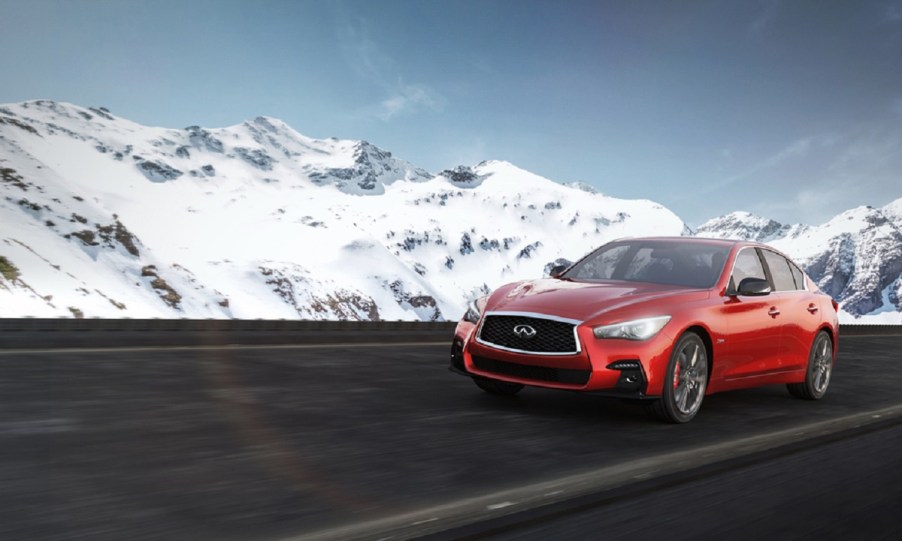 A red 2017 Infiniti Q50 drives through a snowy mountain pass.